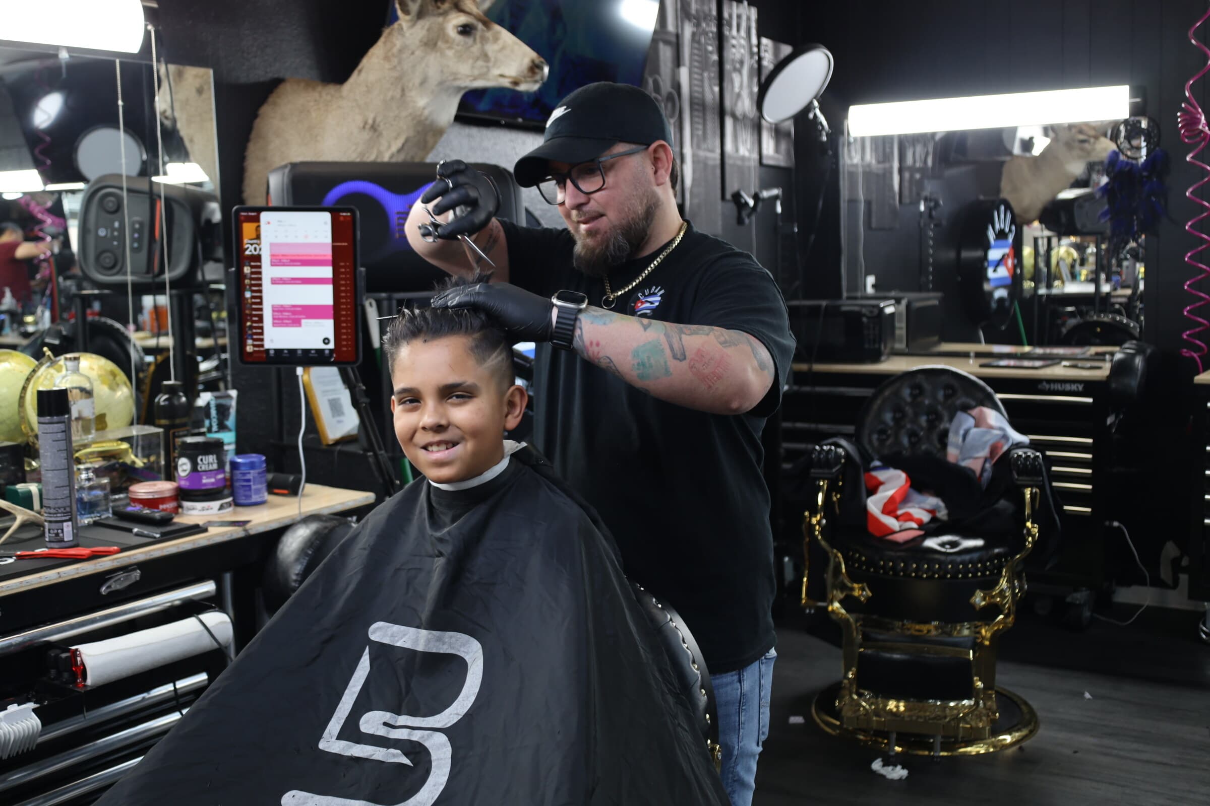A young client grinning in the chair while Adriano cuts his hair at Tu Barber Cubanito in Brighton, Colorado